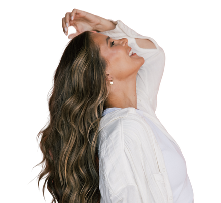 Smiling woman in profile with long wavy hair, leaning back and wearing a white shirt and small earring.