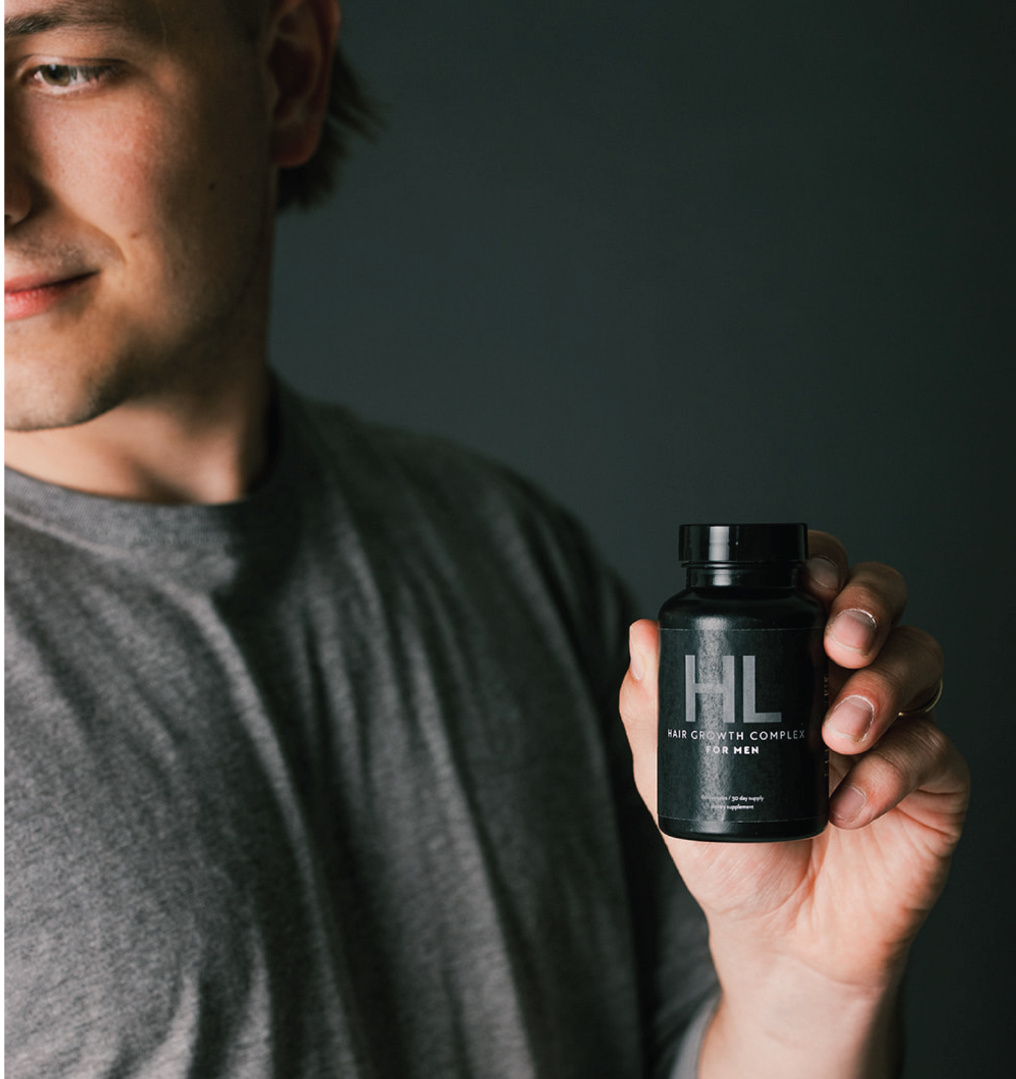 Man holding Black bottle of HAIRLOVE hair growth complex for men, daily hair vitamin with a soft smile